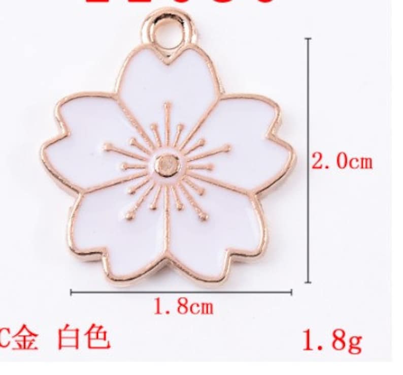 May include: Gold-tone metal charm with a white enamel cherry blossom design. The charm measures 1.8 inches in diameter and weighs 1.8 grams.