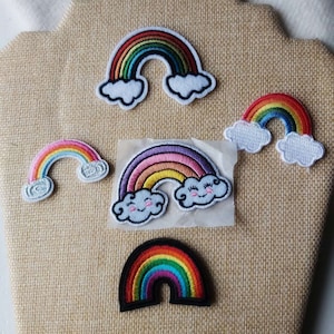 Peut inclure: Cinq patchs brodés en forme d'arc-en-ciel avec des nuages. Les arcs-en-ciel sont de couleurs et de styles différents. Certains des nuages ont des visages.