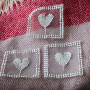 May include: Three white lace appliques with embroidered hearts on a pink and white striped fabric background.