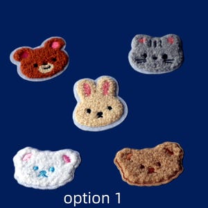 May include: Five embroidered animal patches: a brown bear, a grey cat, a white bear, a tan bunny, and a brown bear. Each patch has a white border against a dark blue background. The text "option 1" is at the bottom of the image.