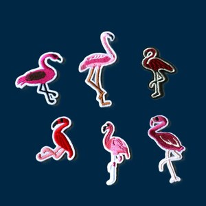 May include: A collection of six embroidered flamingo patches in various shades of pink and red. Each patch features a distinct flamingo pose, including standing, walking, and resting positions, all outlined with a white border for clear definition.