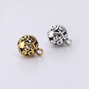 May include: Two ornate metal charms, one gold and one silver, with a delicate filigree design. Each charm has a small loop for attaching to a necklace or bracelet.