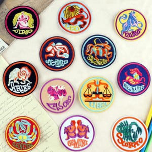 May include: Twelve round embroidered iron-on patches featuring the astrological signs. Each patch has a different colour background and features a unique design of the zodiac symbol. The signs include Aries, Taurus, Gemini, Cancer, Leo, Virgo, Libra, Scorpio, Sagittarius, Capricorn, Aquarius, and Pisces.