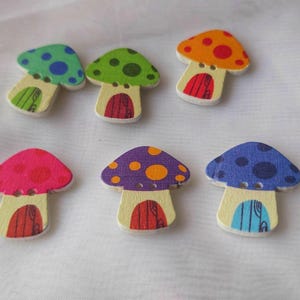 May include: Six wooden mushroom-shaped buttons with colourful caps and door-like bases. The caps are painted in various colours, including green, orange, pink, purple, and blue, with contrasting polka dots. The bases are a light wood colour.