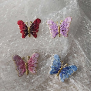 May include: Four embroidered butterfly patches in different colours: red, purple, pink, and blue. The butterflies have gold accents and are on a white background.