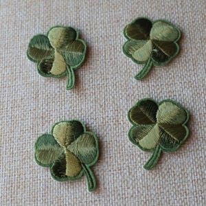 May include: Four green four-leaf clover patches with a gold outline. The patches are embroidered and have a textured look.