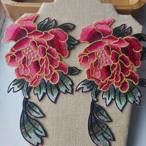 May include: Two pink and green embroidered fabric flower patches with gold accents. The flowers are peonies with detailed stitching.