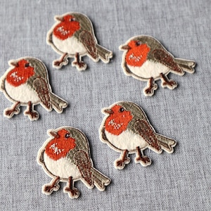 May include: Five embroidered patches of robins. Each patch features a bird with a red breast, white belly, brown wings and tail, and a gray head. The patches are on a gray fabric background.