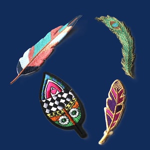May include: Four embroidered patches shaped like feathers and leaves. One is a long, multi-coloured feather with teal, orange, and black. Another is a green peacock feather. A third is a wide, pointed leaf with a black and white checkered pattern. The fourth is a small, purple and gold feather.