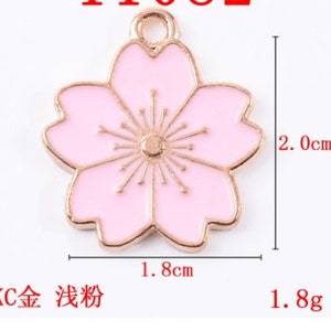 May include: A gold-tone charm with a pink enamel cherry blossom design. The charm measures 1.8 inches in width and 2 inches in height.