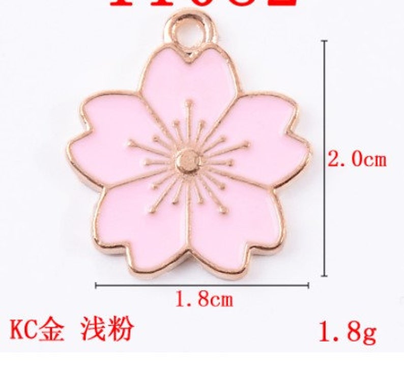 May include: A gold-tone charm with a pink enamel cherry blossom design. The charm measures 1.8 inches in width and 2 inches in height.