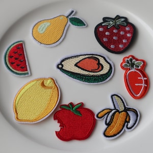 May include: A set of embroidered iron-on patches featuring various fruits and vegetables, including a watermelon, pear, strawberry, avocado, lemon, carrot, banana, and apple.