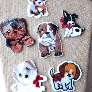 Peut inclure: Six patchs brodés thermocollants représentant différentes races de chiens. Les patchs sont blancs avec des broderies brunes, noires et rouges. Les chiens sont tous en position assise ou debout.