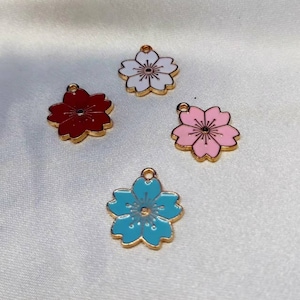 May include: Four gold-colored metal charms shaped like cherry blossoms. The charms are painted in different colors: white, red, pink, and blue.