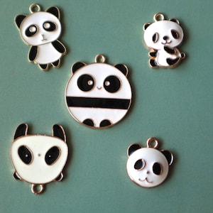 May include: Five panda bear charms in different designs. Each charm is white with black detailing and a gold-coloured border. The pandas have black eyes and ears, with a small loop at the top for attaching to jewellery.