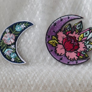 May include: Two embroidered crescent moon patches. One is purple with a pink flower and crystals. The other is blue with a floral design.