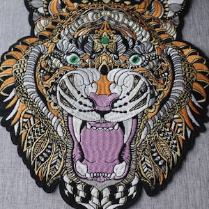 May include: Embroidered tiger patch with detailed design. The patch depicts a roaring tiger in orange, white, grey, and black. The tiger's mouth is open, showing a pink interior. The patch has an ornate pattern, with intricate detailing throughout.