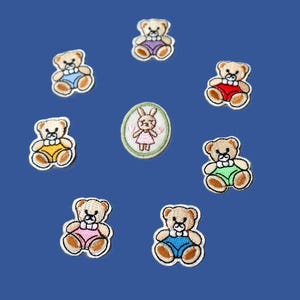 May include: Embroidered patches of teddy bears in different coloured shorts and a bunny in a dress. The patches are arranged in a circular pattern on a blue background. The teddy bears are light brown and wear blue, red, yellow, green, and pink shorts.