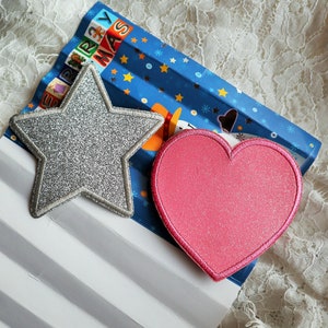 May include: A silver glitter star and a pink glitter heart on a blue and white striped background with the text "Merry Christmas".