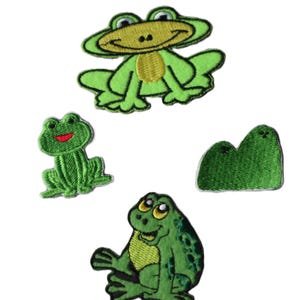 May include: Four green frog embroidered iron-on patches. Two of the frogs are sitting with their legs outstretched, one is sitting with its legs tucked under its body, and the last is a simple outline of a frog.