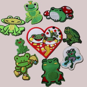 May include: A set of nine embroidered iron-on patches featuring frogs in various poses and designs. The patches are colourful and whimsical, with a variety of colours including green, red, yellow, and white.
