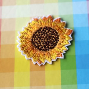 Könnte beinhalten: Ein gestickter Sonnenblumen-Patch in Gelb und Braun mit weißen Nähten an den Rändern.