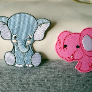 May include: Two embroidered elephant patches. One is light blue with grey accents, in a seated pose. The other is pink with a white ear and a stitched outline. Ideal for craft projects, these patches are decorative.