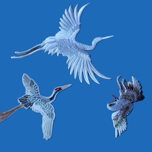 May include: Three embroidered crane patches in flight against a blue background. The cranes feature detailed white and gray feathers, with red accents on their beaks and heads. The patches are likely for sewing or crafting.