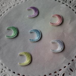 May include: Six colourful crescent moon shaped iron-on patches. The patches are in shades of purple, pink, green, blue, white, and yellow.