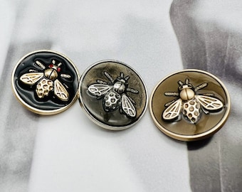 May include: Three metal buttons with a bee design. The buttons are black, silver, and gold. The bees are detailed with black, silver, and gold accents.