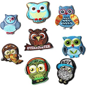 May include: A selection of embroidered owl patches in various colours and designs. The patches feature owls with different expressions, wearing accessories like aviator goggles, headphones, and baseball caps. Some patches have text that reads "OVERNIGHTER".