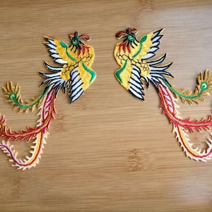 May include: Two embroidered phoenixes with red, yellow, green and white thread. The phoenixes are facing opposite directions and have long, flowing tails.