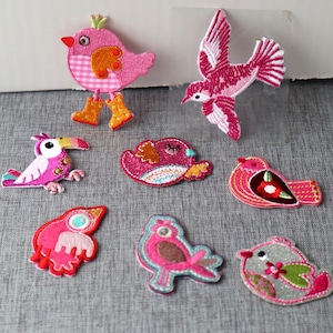 Peut inclure: Assortiment de patchs brodés colorés à repasser représentant différents motifs d'oiseaux. Les patchs comprennent un oiseau rose avec une couronne, un oiseau rose aux ailes déployées, un toucan rose, un oiseau rose aux yeux fermés, un oiseau rose avec un cœur rouge, un oiseau rose avec des accents bruns, un oiseau gris avec des accents verts et un oiseau rose avec un cœur rouge.