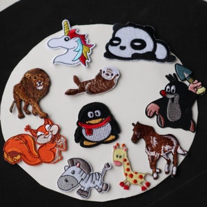 May include: A set of ten colorful embroidered iron-on patches featuring various animals, including a unicorn, a panda, a lion, a squirrel, a penguin, a zebra, a giraffe, an otter, a cartoon character, and a ladybug.