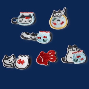 May include: A collection of six embroidered patches featuring black and white cats and goldfish in bowls. The designs include a cat in a mug, a cat perched on a bowl, a cat lying by a bowl, a red goldfish, and cats interacting with fishbowls.