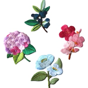 Könnte beinhalten: Vier gestickte Bügelbilder mit Blumenmotiven. Die Patches beinhalten einen rosa Hortensienstrauß, eine blaue Blume, eine rosa Blume und einen blauen Beerenzweig.