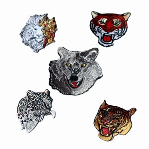 Peut inclure: Écussons brodés représentant des visages d'animaux : un lion, un tigre, un loup, un léopard des neiges et un tigre. Les écussons présentent des coutures détaillées et des couleurs vives, sur fond blanc.