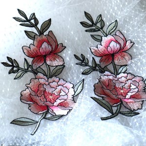 May include: Two embroidered floral appliques featuring pink and green flowers on a white mesh background.