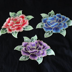 May include: Three embroidered flower patches in pink, blue, and purple. The flowers are detailed with gold thread and have green leaves.