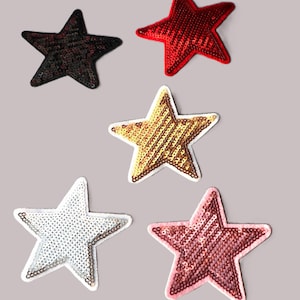 Peut inclure: Cinq patchs thermocollants en forme d'étoile avec des embellissements en paillettes. Les étoiles sont en noir, rouge, or, blanc et rose.