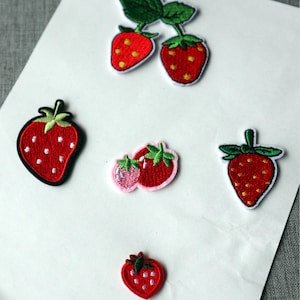 May include: Embroidered strawberry patches in different sizes and styles. The patches show red strawberries with white seeds and green leaves. Some have a black border, others a white border. Ideal for clothing.