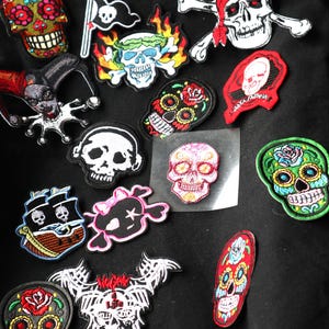 Peut inclure: Un sac fourre-tout noir avec une variété de patchs brodés colorés représentant des crânes, des pirates et d'autres motifs. Les patchs sont cousus sur le sac de manière aléatoire.
