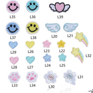 May include: A set of 15 iron-on patches featuring various designs, including smiley faces, hearts, stars, wings, paw prints, and flowers. The patches are in various colors, including pink, blue, yellow, and white.