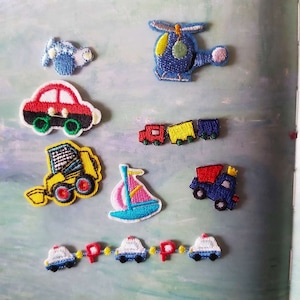 May include: A set of ten embroidered iron-on patches featuring various vehicles, including a red car, a blue helicopter, a yellow bulldozer, a blue dump truck, a pink sailboat, a red train, and three blue police cars.