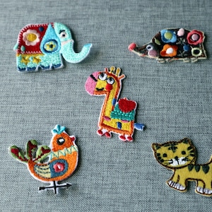 May include: A selection of embroidered animal patches. The patches depict an elephant, hedgehog, giraffe, bird, and tiger. They are brightly coloured and intricately stitched, ideal for decorating clothing or accessories.