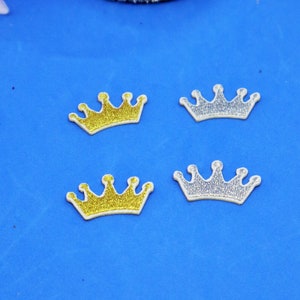 May include: Four gold and silver crown-shaped iron-on patches on a blue background.