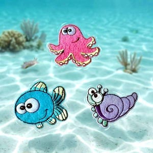 May include: Three embroidered patches featuring cartoon sea creatures: a pink octopus with large eyes, a bright blue fish with striped fins, and a purple spiral-shelled snail with antennae, all displayed against a clear, shallow sandy ocean floor.