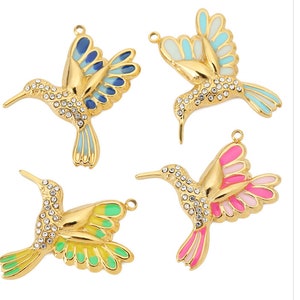 May include: Four gold-tone metal hummingbird charms, each featuring clear rhinestones on the head and neck, with enamel-filled wings and tails in blue, light blue, green, and pink colour variations, each with a small jump ring at the top.