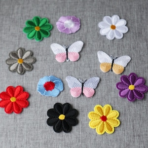May include: Assortment of embroidered iron-on patches featuring flowers, butterflies, and a variety of colours. The patches are perfect for adding a unique touch to clothing, bags, or other fabric items.
