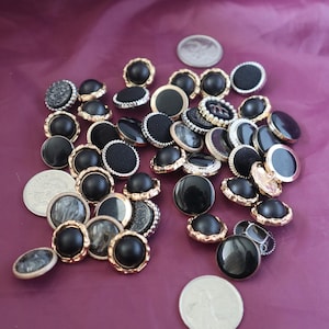 May include: A selection of buttons in various designs. The buttons have black, gold, and silver details, with some having textured surfaces. Some buttons have a shiny finish, while others are fabric-covered. A few coins are also visible.